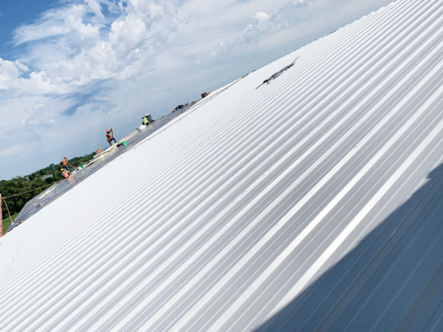 a wide expanse of metal roofing with workers in the distance